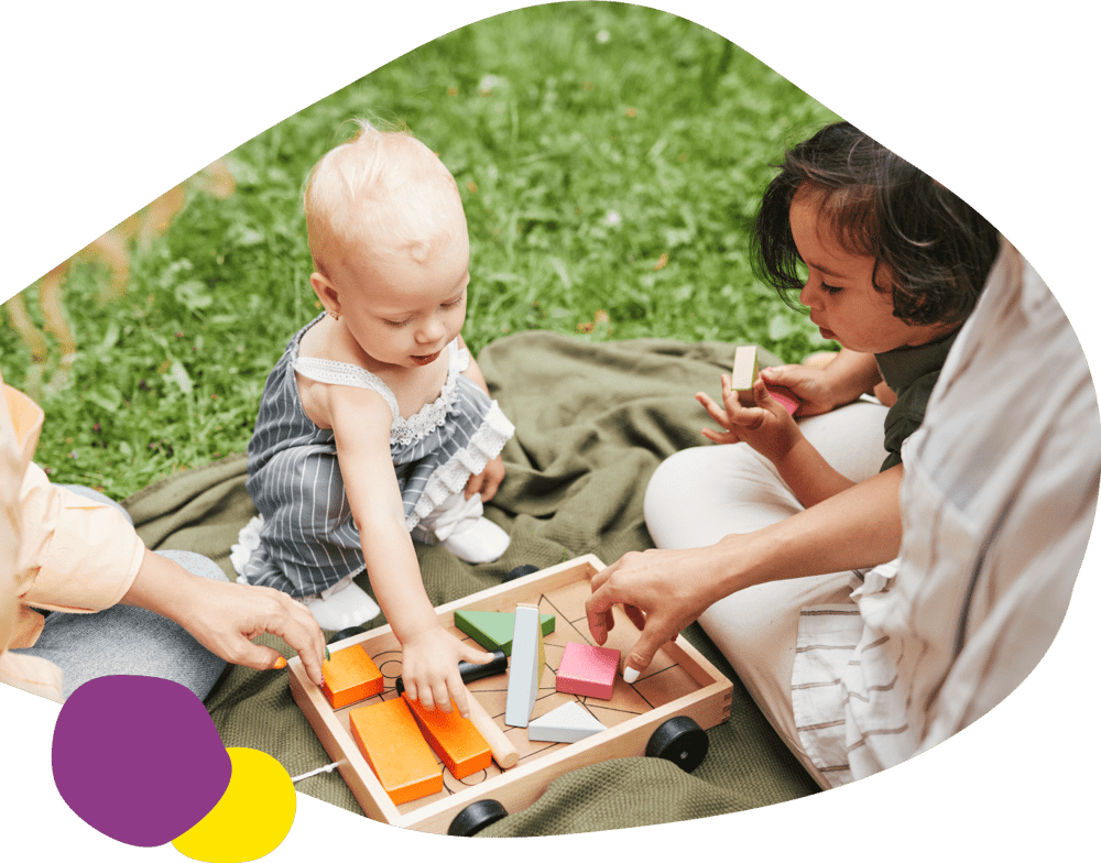 Small baby playing with blocks along with a toddler in grass field